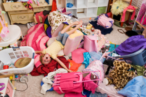 A child lying upon a pile of clothes and toys in a chaotic messy bedroom