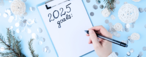 A hand holding a pen is writing "2025 Goals" on a piece of paper